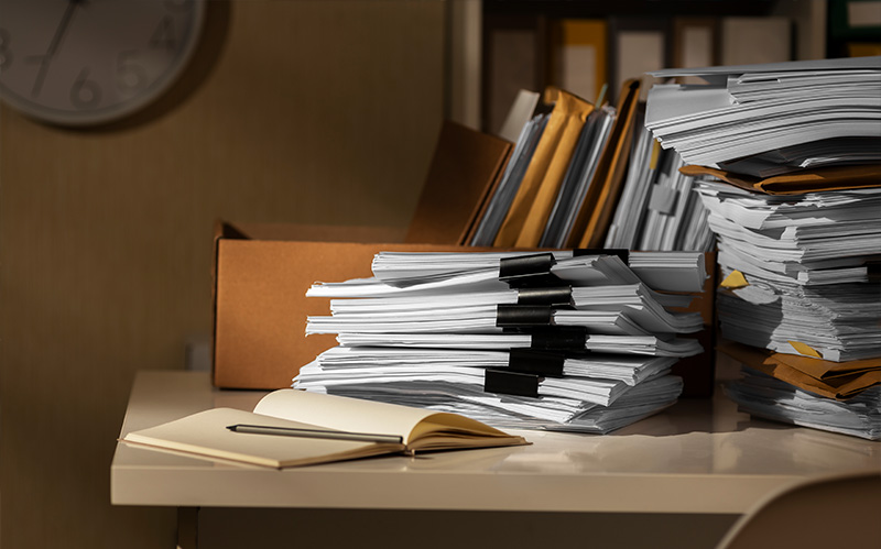 Large stacks of paper corporate files on desk.